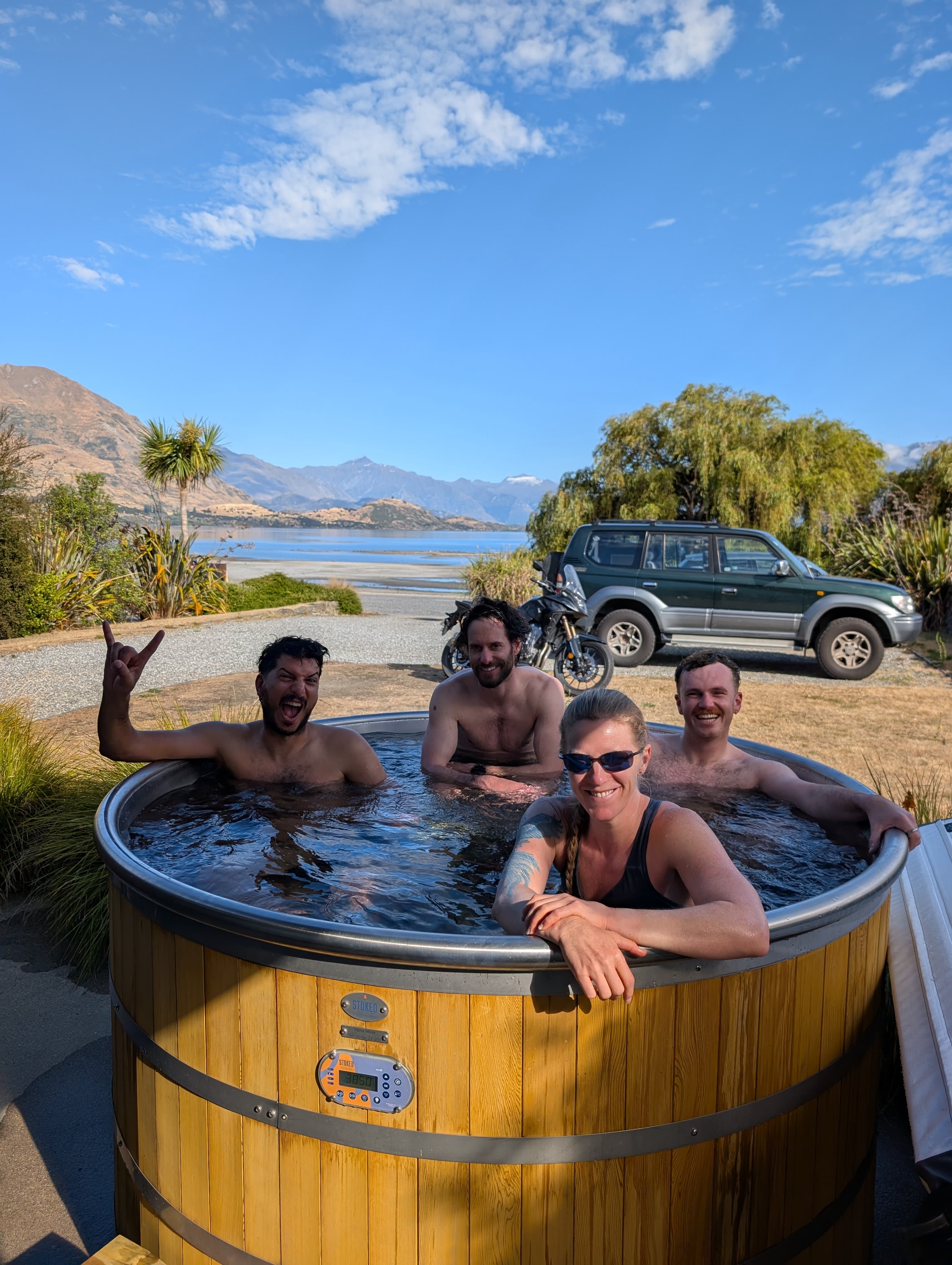 Four friends relaxing in a hot tub at The Balance Base with Lake Wānaka and mountains in the background.